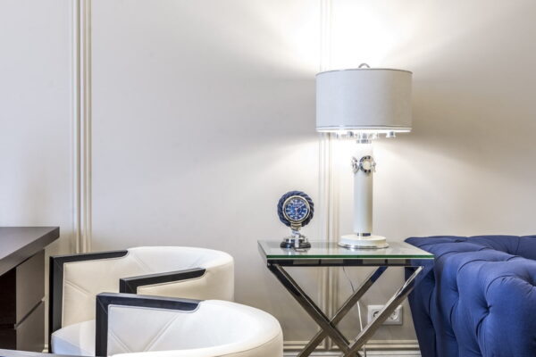 Interior of contemporary living room with small table and lamp near sofa and armchairs