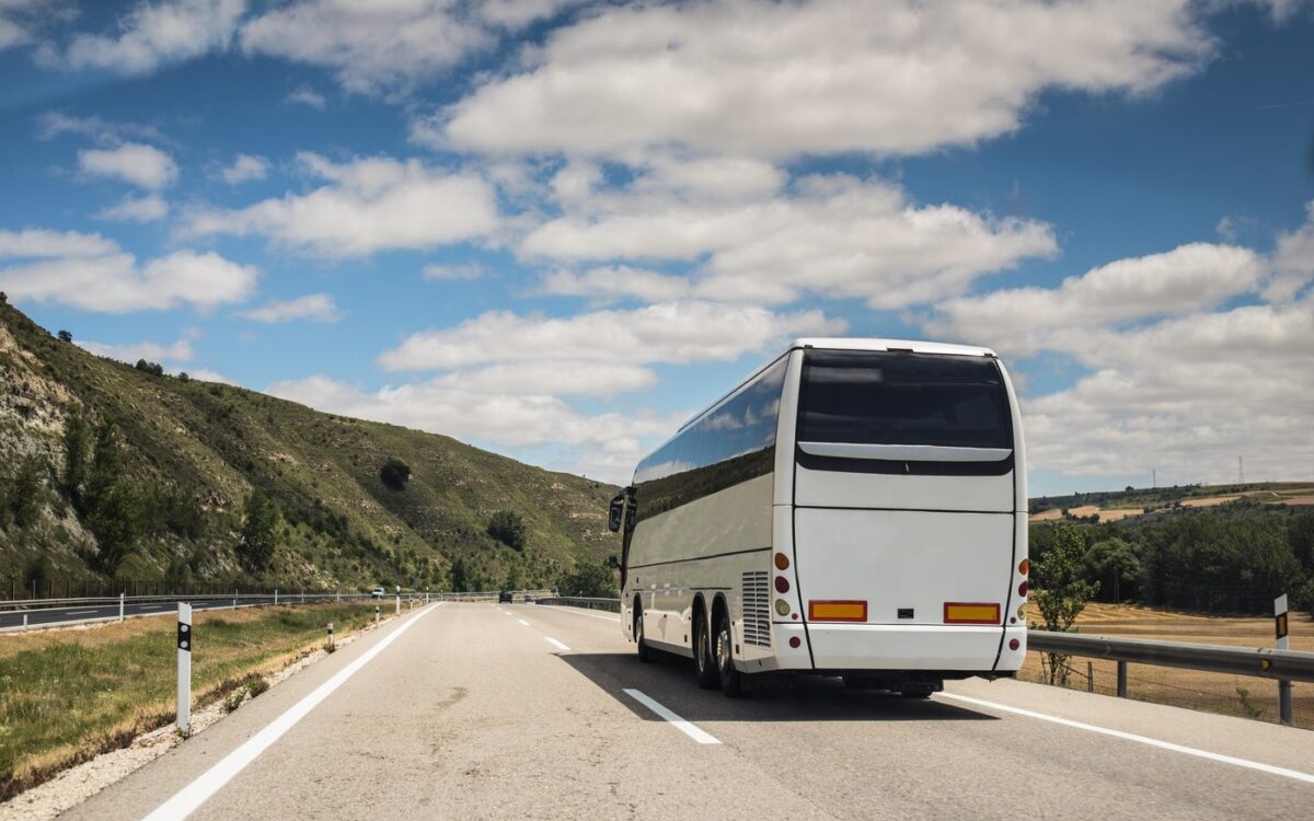 Autocar alb pe autostradă prin peisaj deluros