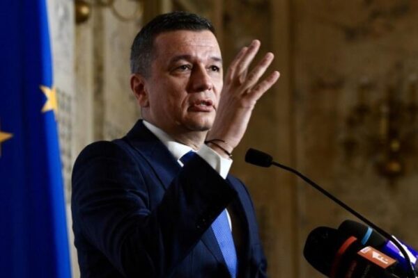 Bărbat în costum vorbind la podium, steagul UE